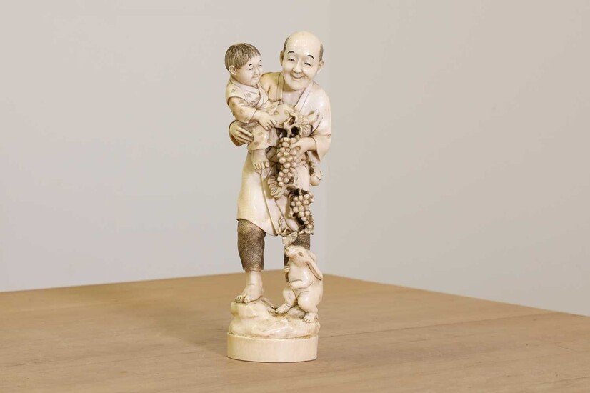 A Japanese solid carved ivory figure of a man carrying a child