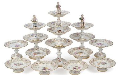A Meissen composite part dessert service, late 19th century, hand-painted with blossoming flowers and butterflies and with alternating reticulated lattice and cartouche borders, comprising: four two-tiered cake stands, two surmounted by a figural...