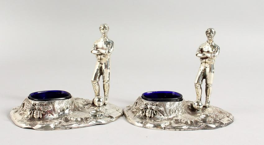 A PAIR OF TABLE SALTS, modelled as early footballing