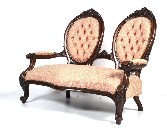 A Victorian carved mahogany two-seat parlor sofa. Of serpentine form, upholstered in pale peach/pink damask, with twin oval shaped foliate carved button backs, with scroll arms, on cabriole legs, L135cm x D62cm x H102cm