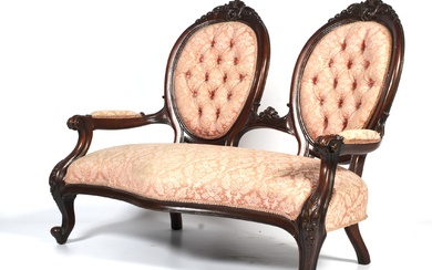 A Victorian carved mahogany two-seat parlor sofa. Of serpentine form, upholstered in pale peach/pink damask, with twin oval shaped foliate carved button backs, with scroll arms, on cabriole legs, L135cm x D62cm x H102cm
