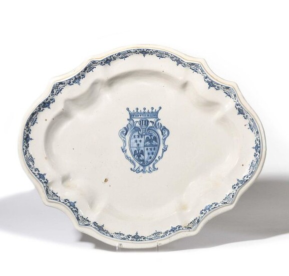 Midi Oval dish with contoured rim in earthenware with blue monochrome decoration in the center of a coat of arms in a shield under a crown and foliated scrolls on the rim. 18th century. L. 42 cm