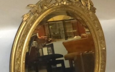 Miroir ovale en bois et stuc doré à décor de lauriers et rubans. XIXe siècle....