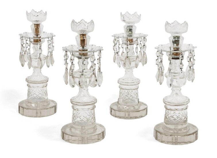 A set of four Regency clear cut-glass candlesticks, with crenulated sconces and teardrop lustres leading to urn shaped bodies atop plinth supports, terminating in octadecagon bases, 39cm high (4)