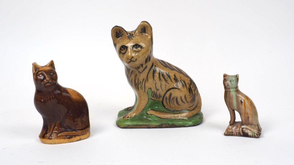 A glazed pottery cat, 19th century, seated on a naturalistic base, unmarked, 17.5cm high, together with a pottery cat modelled as a money bank, mid 19th century, possibly by Methvens of Kircaldy, unmarked, 12cm high, and a glazed creamware figure...