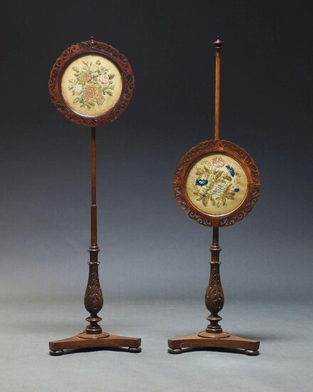 A pair of Victorian mahogany pole screens, with circular fretwork frames and glazed screens, enclosing floral needlework panels, on acanthus carved stand to trefoil base with disc feet (2)