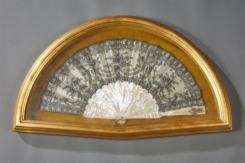 Folded type fan, the strands and frame in mother-of-pearl, silk leaf and black embroidery with openwork decoration of stylized foliage and volutes. The end of a plume decorated with a number.