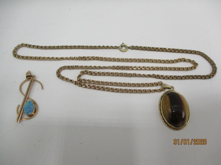 A 9ct gold pendant set with tigers eye on a yellow metal cha...