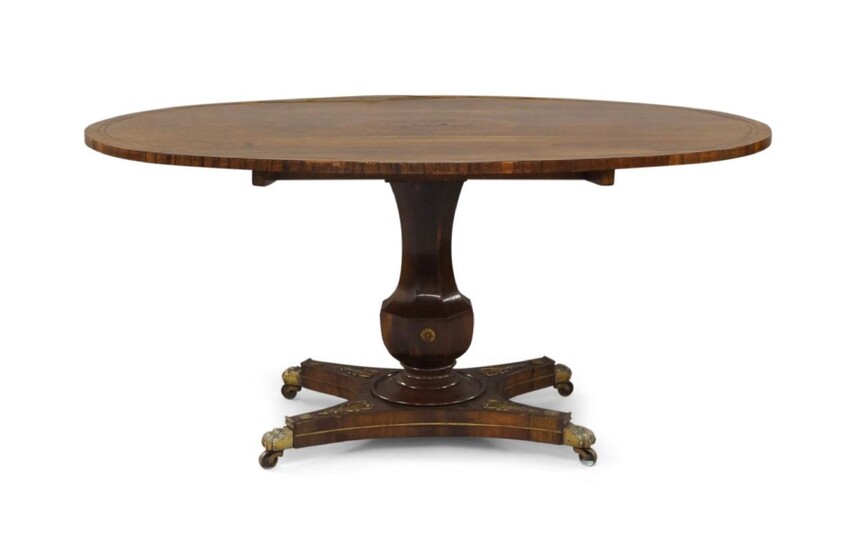 A Regency rosewood tilt top breakfast table, the oval top with brass inlay, raised on octagonal baluster shaped column, quadraphite base with gilt metal mounts, paw caps and castors, 68cm high, 147cm wide, 108cm deep