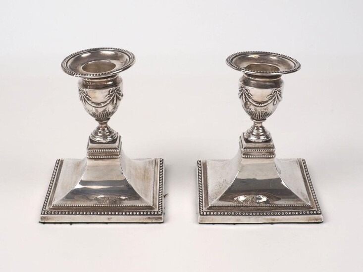 A pair of Edwardian silver candlesticks, London, 1900, William Hutton & Sons, designed with garland-decorated urn-shaped capitals to square feet with beaded borders, 10cm high (2)