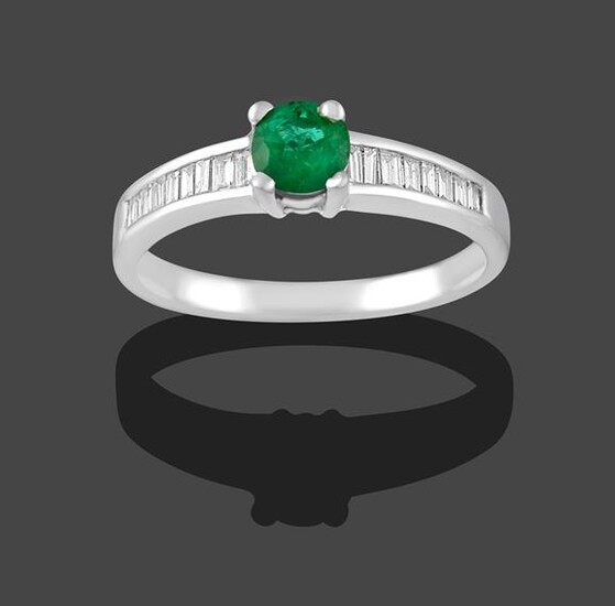 An Emerald and Diamond Ring, the round cut emerald in a white claw setting to baguette cut...