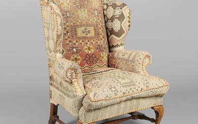 A GEORGE II STYLE WALNUT WING ARMCHAIR. upholstered in a kel...