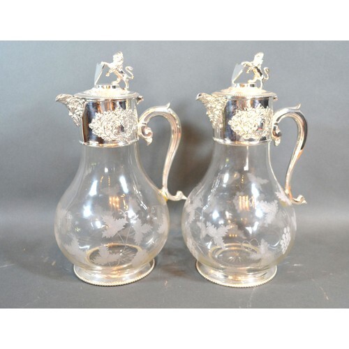 A pair of silver plated and engraved glass claret jugs, each...