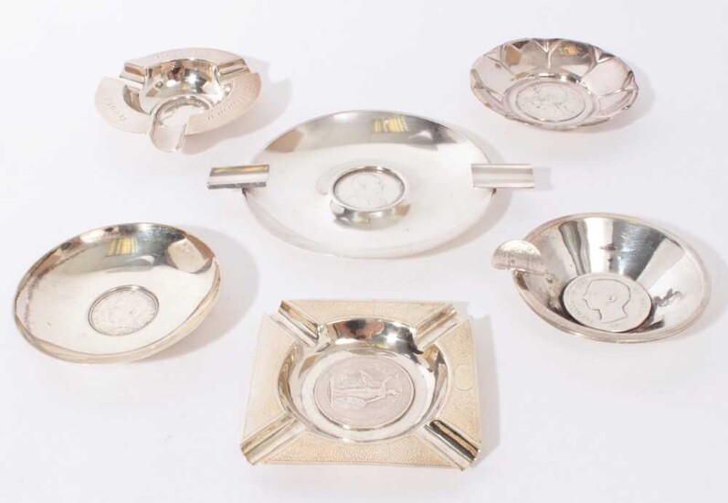 Group of six Continental silver and white metal ashtrays and pin dishes, each one set centrally with a coin or medallion, all at 11.5oz (6)