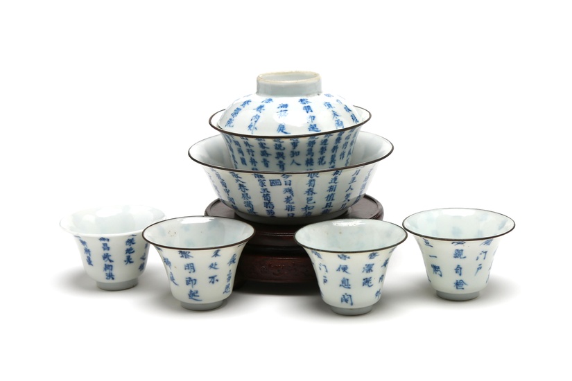 A blue and white porcelain tea set comprising four teacups, one bowl and a covered teacup each painted with Chinese characters