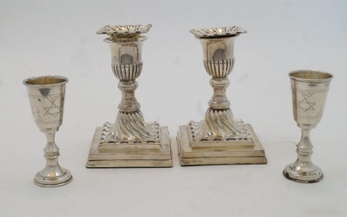 A pair of Victorian filled silver candlesticks, Sheffield, 1888, Hawksworth, Eyre & Co Ltd, with scalloped and gadrooned sconce above knopped stem on stepped square bases, approx. 12cm high; together with a pair of silver Kiddush wine cups, London...