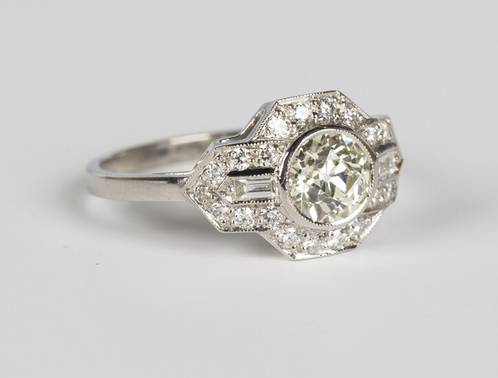 A platinum and diamond ring, collet set with the principal circular cut diamond within a shaped surr