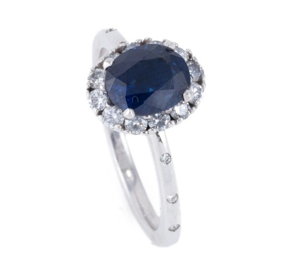 AN 18CT WHITE GOLD SAPPHIRE AND DIAMOND RING; featuring an oval cut mid dark blue sapphire of approx. 1.65ct with a halo of 12 round...