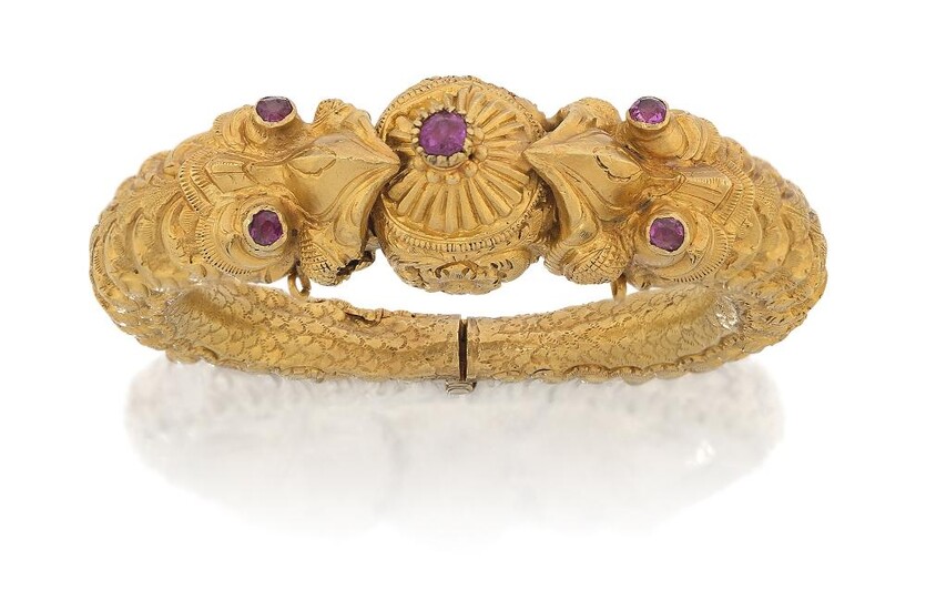 An early 20th century gold, double-headed chimera hinged bangle, of shaped circular form, the heads and clasp collet-set with five rubies to chased, tapering sides with hinge at base, unmarked clasp defective as appears in fixed position, inner...