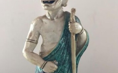 1 statuette en faience de kutani à couverte verte et managanèse, figurant 1 arhat debout son bâton de pélerin dans la main gauche, sa cloche dans la main droite. Manques aux deux boucles d'oreille.
