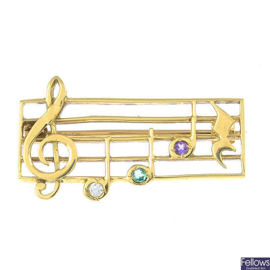 An 18ct gold brilliant-cut diamond and circular-shape gem-set musical bar brooch.