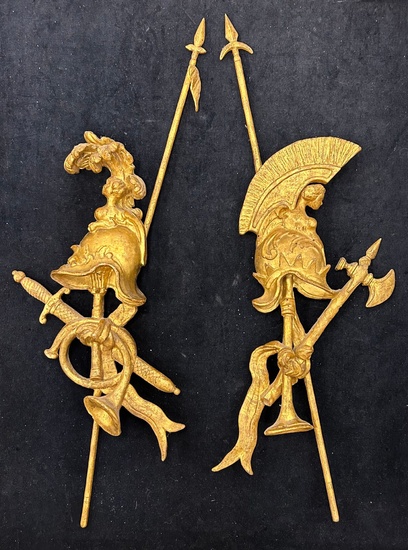 Deux éléments décoratifs d’applique en bois sculpté et doré à motifs d’attributs guerriers. Hauteur: 70...