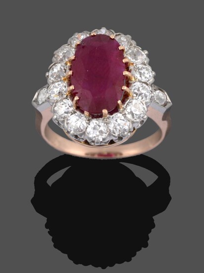 A Ruby and Diamond Cluster Ring, the oval cut ruby in a yellow claw setting within a border of...