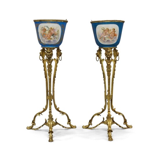 A pair of French gilt-bronze mounted Sevres jardinieres-on-stands, first half 20th century, the jardinieres painted with emblematic of music and the arts, the reverse flowers, the stands with lion-head mounts and ring handles, on foliate triform...