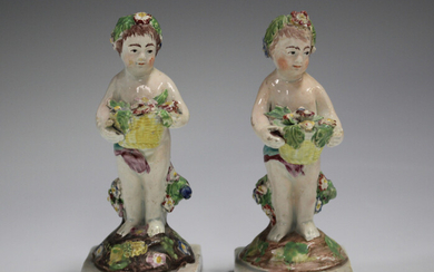 A pair of Staffordshire pearlware putti, first half 19th century, each modelled standing holding a b