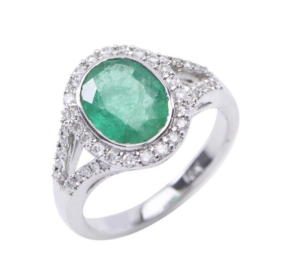 AN EMERALD AND DIAMOND CLUSTER RING - Of Art Deco design, featuring an oval cut emerald estimated 2.20cts, in a surround of round br...