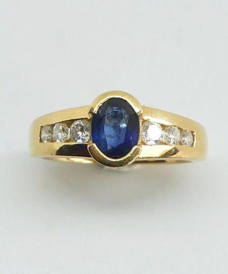 RING in yellow gold set in a half-closed setting with a facetted oval sapphire, the setting enhanced on either side by a line of diamonds. Gross weight 6.79 g TDD 51