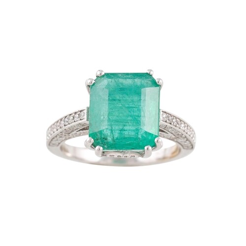 AN EMERALD SOLITAIRE RING, with diamond shoulders, mounted i...