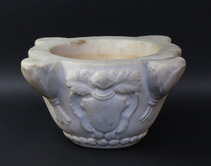 White marble mortar with four ribs in foliage sheaths. The body is decorated with an escutcheon topped by a helmet. Frieze of pearls on the base. 18TH, 19TH CENTURY. Height 16 cm. Max. diameter 33,5 cm