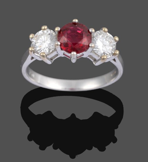 An 18 Carat White Gold Ruby and Diamond Three Stone Ring, a round cut ruby sits between two...