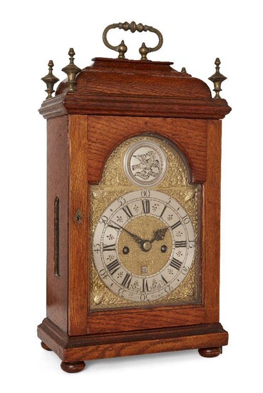 An oak striking table clock, by Joseph Smith of Barthomley, early to mid 18th century, the oak case with brass swing handle and urn finials to top, over arched glazed door on plinth base with bun feet, with glazed panels to sides and reverse, the...