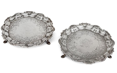 A pair of George III silver waiters, London, 1749, Hugh Mills, of shaped circular form with a cast shell and scroll border, each raised on three pad feet and chased with floral and fruit motifs around a central armorial 17.7cm dia., total weight...