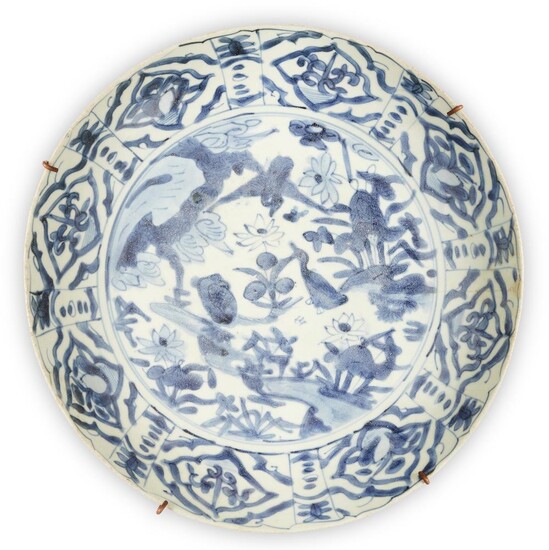 A large Chinese Swatow blue and white 'duck' charger, Ming dynasty, 16th century, painted to the central medallion with ducks among lotus pond, surrounded by a band of floral cartouches to the rim, mounted with a metal hanging rack, 38.5cm diameter...