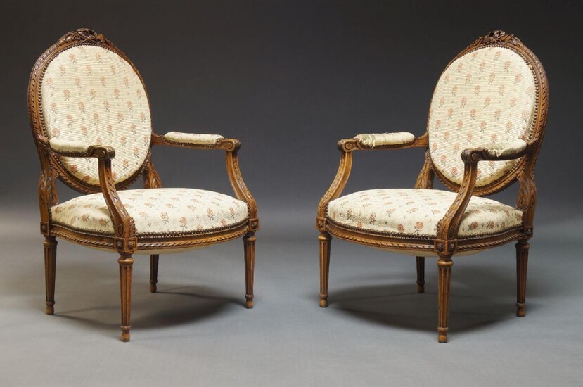 A pair of Louis XVI style fauteuils, first half 20th Century, the oval backs surmount with carved ribbon and foliate decoration, upholstered in floral pattern fabric, on tapering fluted legs with ovoid feet (2)