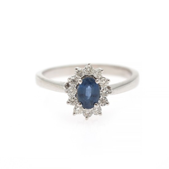 A sapphire and diamond ring set with a sapphire encircled by numerous diamonds, mounted in 14k white gold. Size 55.