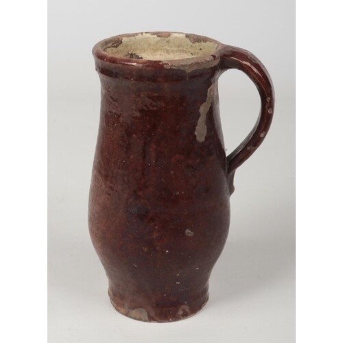 A 17th century brown glazed earthenware mug with plain strap...