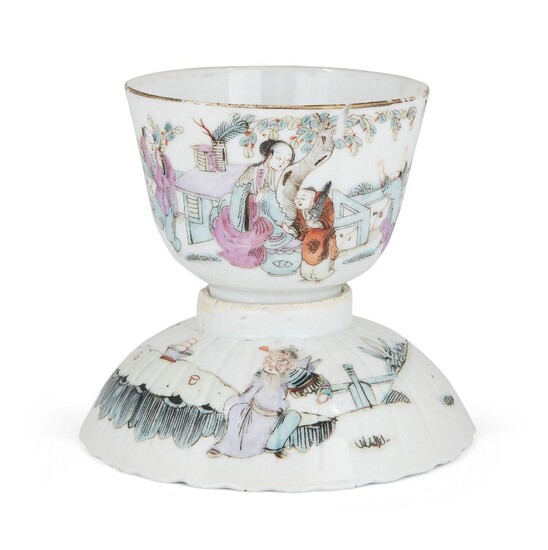 A Chinese porcelain famille rose tea bowl and a fluted bowl cover, early 20th century, the tea bowl painted with a lady sat at a table whilst children play in the garden, the stand decorated with two figures in conversation, both with...