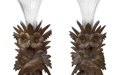 A pair of Swiss 'Black Forest' wood vase stands, c.1900, each carved with two pheasants standing before leaves and flowers supporting glass trumpet shaped vases, 50.5cm high (2)