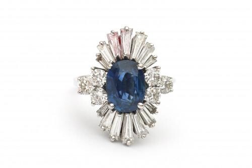 An 18 carat white gold sapphire and diamond cluster ring. Featuring an oval cut blue sapphire of ca. 2.40 ct. surrounded by fourteen baguette cut tapered diamonds and six brilliant cut diamonds, in total ca. 2.90 ct., ca . G-H, ca. VS. Gross weight:...
