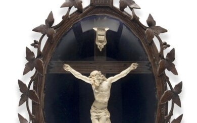 A Swiss Black Forest carved wood and meerschaum Corpus Christi, c.1920, the oval glazed frame with leaves and surmounted by a cross, the crucifix mounted on cobalt blue velvet, 65cm high, 40cm wide