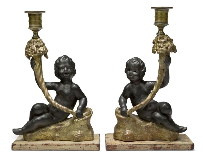 A pair of Regency gilt and black painted plaster candlesticks, early 19th century, in the form of putti holding cornucopia, on later painted metal bases, 27cm high, the bases 16 x 7.5cm (2)