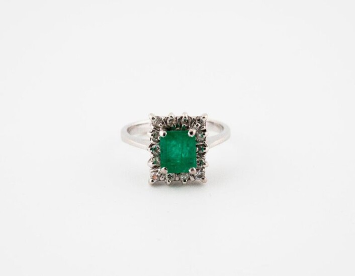 A white gold ring (750) centered by a rectangular emerald in a setting of small brilliants, in claw setting.