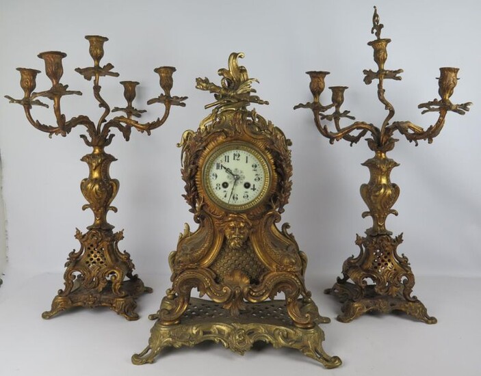Gilded bronze mantel set with rocaille decoration and a man's mask comprising a clock and a pair of five-light candelabra.
