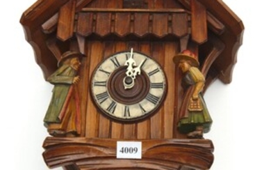 A CARVED AND PAINTED WOODEN CUCKOO CLOCK, IN THE FORM OF A CABIN, WITH A MALE AND FEMALE FIGURE STANDING AT THE FRONT, ONE WEIGHT ON...