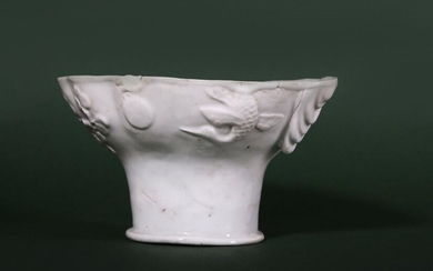A LARGE CHINESE BLANC-DE-CHINE LIBATION CUP. Qing Dynasty, 18th Century. The flared body with a lobed rim moulded to one side with a dragon emerging from clouds and reaching out for a flaming pearl, the reverse with a crane flying towards the sun and...