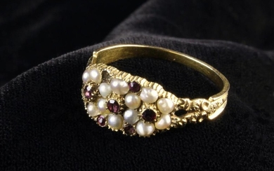 A Victorian Gold Ring set with a cluster of seed pearls and garnets, the split shoulders carved with